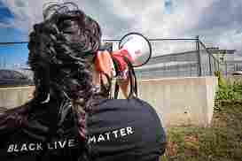 Image of a protester, wearing a Black Lives Matter shirt, speaking through a bullhorn outside Carswell.