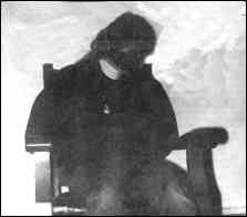 Photo shows dejected woman, restrained, sitting in a chair.