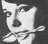 Close-up photo of a young woman's face; a large spoon is clenched in her teeth by its handle.