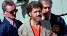 Photo shows Ted Kaczynski with federal officers on either side.