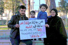 Photo shows a man, a woman and two small children holding a sign reading "We are one of 760,000 families in Idlib."
