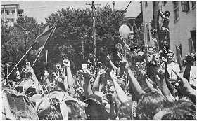 Photo shows an angry crowd of young people gathered near a university building. All fists are raised.
