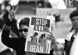 Photo shows a person giving a V-sign and holding a sign that reads, "Stop killing in Iran."