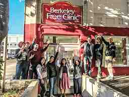 A color painting shows a group of about 15 people in front of the Berkeley Free Clinic, most saluting with raised fists.