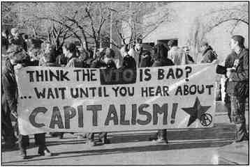 Photo shows a group of protesters in Seattle. Banner reads, "Think WTO is bad? Wait until you hear about capitalism!"
