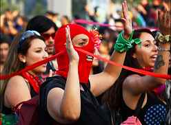 Photo shows women in a demonstration, centering on one with a red mask.