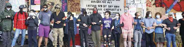 A photo shows a line of masked Seattle protesters with arms linked, all facing the camera.