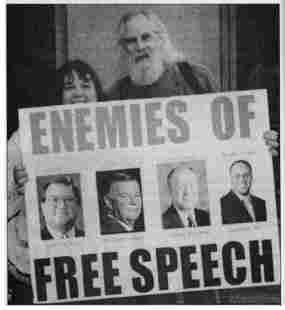 photo of Ron Sakolsky with poster showing images of four mass media executives. Headline reads, "Enemies of Free Speech."