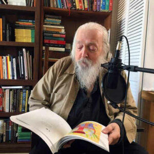 a color photo of an elderly Peter Lamborn Wilson with a microphone reading from Temporary Autonomous Zone, Photo by Chris Funkhouser