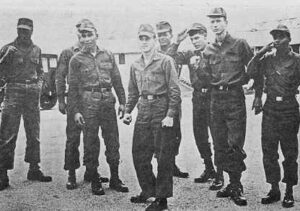 A photo shows a racially-mixed group of 8 U.S. Army troops. All bear angry expressions, many make fists or other aggressive gestures.