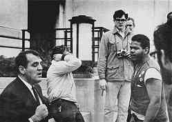 photo shows a suited executive with clenched fists at left. He is confronted by four angry young men at right.