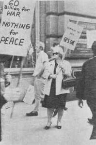 Photo shows a small anti-war protest. Signs read "60 billion for war, Nothing for peace" and "GIs die"