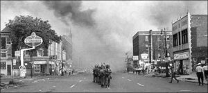 National Guard troops mass in Detroit street during June 1967 rebellion; smoke dominates background.
